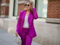 Elegancka kobieta w fuksjowym garniturze i błyszczącym topie, z okularami przeciwsłonecznymi. Idealna stylizacja, jak się ubrać na imprezę w stylu lat 50.
