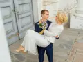 Pan młody niesie pannę młodą na rękach. Zastanawiasz się nad skutkami spóźnienia się z rezerwacją fotografa? Dlaczego 18 miesięcy to minimum?