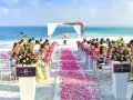 Piękna plażowa ceremonia ślubna. Kwiaty i płatki róż tworzą romantyczną ścieżkę. Goście siedzą na białych krzesłach, a ocean w tle.