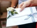 Dłoń trzyma białą kopertę z błękitną wstążką i ozdobnym kwiatkiem. Rozważasz skutki wręczenia pustej koperty lub zbyt małej kwoty? Opinie i etyka są tu kluczowe.