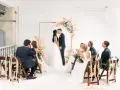 Ślubna ceremonia z pocałunkiem pary młodej. Goście siedzą na udekorowanych krzesłach. Warto wiedzieć, jak wypisać zaproszenie na ślub z dziećmi.