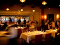 Ciemne, nastrojowe wnętrze restauracji. Goście jedzą przy stołach, kelnerzy krążą. Złe oświetlenie zdjęć jedzenia może zniechęcić gości do publikacji w social mediach.