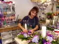 Florystka tworzy nowoczesne kompozycje kwiatowe z liliami i hortensjami. W tle widać półki z wstążkami, jak sprawdzić portfolio florysty pod kątem nowoczesnych kompozycji.