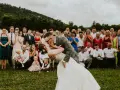 Para młoda całuje się na tle rodziny. Goście czekają na obiad po kościele, a ten pocałunek to idealny sposób, by zająć ich uwagę.