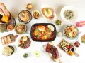 Stół zastawiony różnorodnymi potrawami: mięsa, sałatki, makarony, owoce, pieczywo i desery.