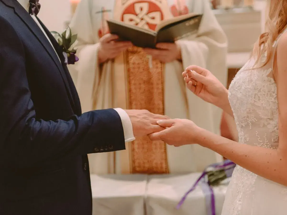 Ceremonia ślubna: pan młody w granatowym garniturze, panna młoda w białej sukni, ksiądz udziela błogosławieństwa. Czy do bycia świadkiem na ślubie trzeba mieć bierzmowanie?