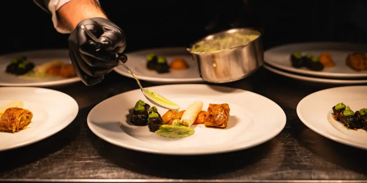 Szef kuchni precyzyjnie serwuje sos, dbając o zasady serwowania dań w stylu "fine dining" na dużych imprezach.