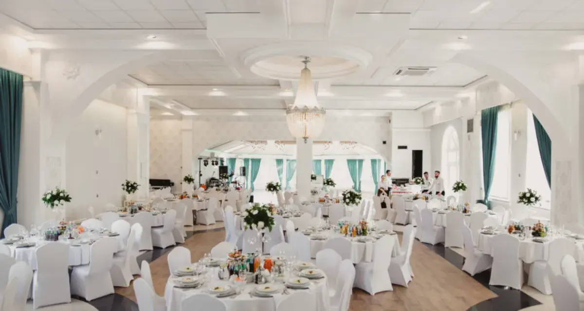 Elegancka sala weselna z białymi pokrowcami na krzesłach, sugerująca rezygnację z modeli tiffany na rzecz prostoty i klasy.