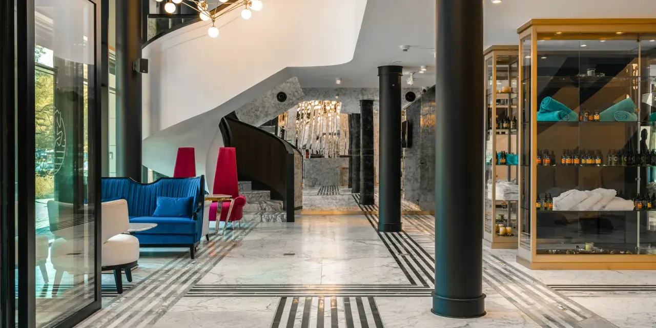 Eleganckie wnętrze bankietowe z niebieską kanapą i czerwonymi fotelami. Przyczyny powrotu do stylistyki art deco w nowoczesnych wnętrzach bankietowych widać w geometrycznych wzorach i luksusowych materiałach.