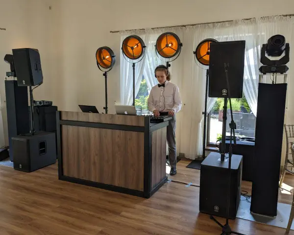 Młody DJ przy konsoli, otoczony sprzętem nagłośnieniowym i oświetleniem. Unikaj błędów w wyborze oprawy muzycznej – DJ czy zespół?