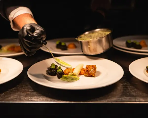 Szef kuchni precyzyjnie serwuje sos, dbając o zasady serwowania dań w stylu "fine dining" na dużych imprezach.