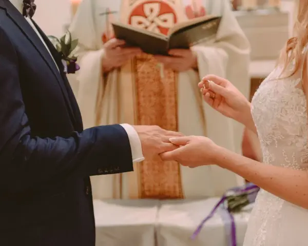 Ceremonia ślubna: pan młody w granatowym garniturze, panna młoda w białej sukni, ksiądz udziela błogosławieństwa. Czy do bycia świadkiem na ślubie trzeba mieć bierzmowanie?
