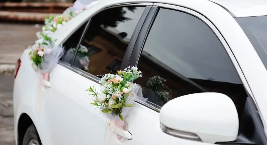 Biały samochód ozdobiony bukietami kwiatów na klamkach i błotniku.