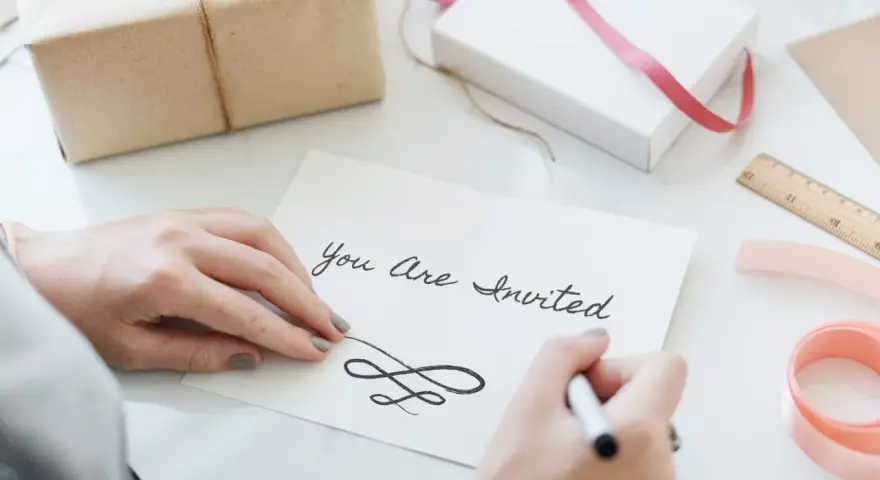 Ręce piszą zaproszenie "You Are Invited". Dowiedz się, jak napisać zaproszenie na urodziny po angielsku.