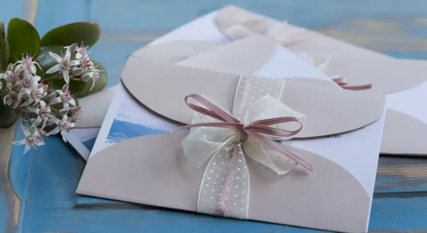 Eleganckie zaproszenia ślubne z różową wstążką. Gdy pojawią się przyczyny rezygnacji gości z udziału w weselu, warto wiedzieć, jak odmówić z klasą.