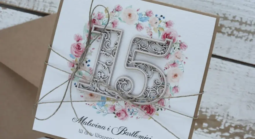 Elegancka kartka z napisem "15 rocznica ślubu" i imionami Malwina i Bartłomiej, ozdobiona kwiatowym wiankiem i sznurkiem.