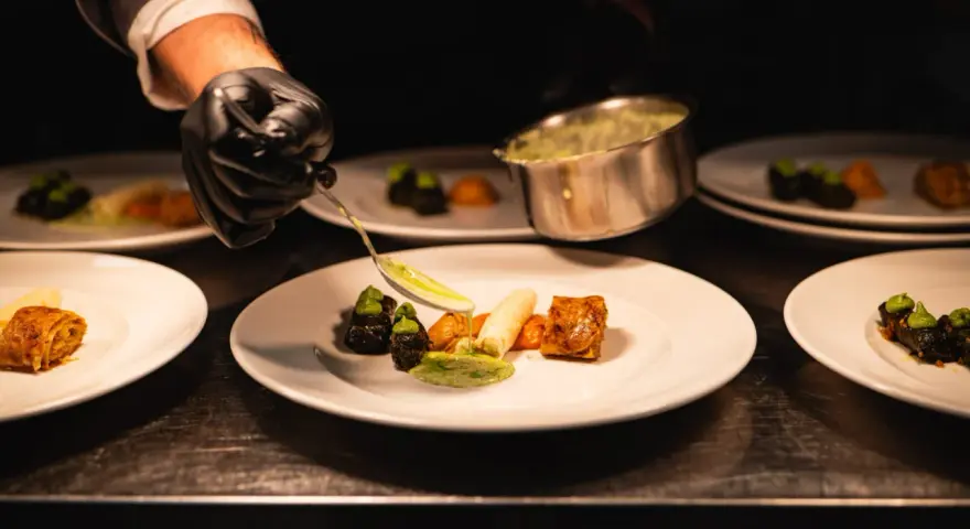 Szef kuchni precyzyjnie serwuje sos, dbając o zasady serwowania dań w stylu "fine dining" na dużych imprezach.