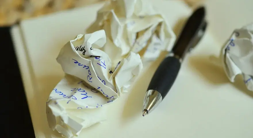 Zgniecione kartki z notatkami i długopis. Ilustruje, jakie są najczęstsze błędy w adresowaniu zaproszeń do par niebędących w małżeństwie.
