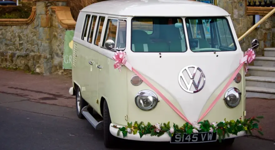 Klasyczny VW Transporter, ozdobiony różową wstążką i kwiatami, gotowy do transportu gości. Zasady dopisywania informacji o noclegu i transporcie dla gości są jasne.