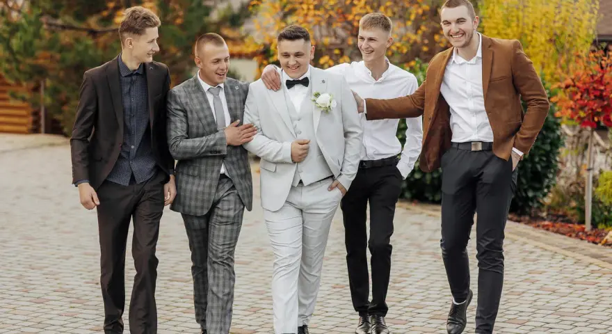 Pięciu mężczyzn w eleganckich stylizacjach, pokazujących, jakie są trendy w stylizacjach męskich dla gości weselnych 2026: garnitury, marynarki i klasyczne koszule.