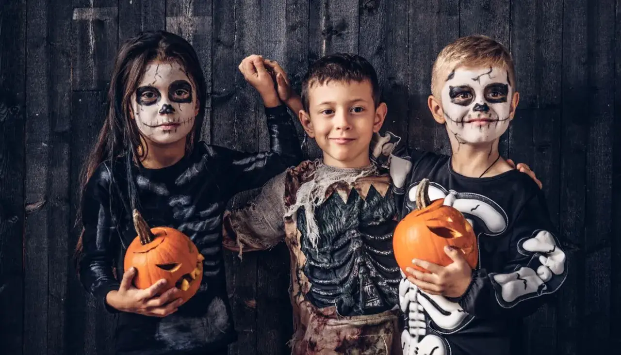Trójka dzieci w przerażających strojach na Halloween, z dyniami w rękach, gotowa na zbieranie słodyczy.