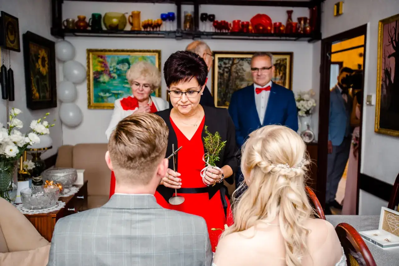 Rodzina celebruje błogosławieństwo w domu, odradzając tradycje. Kobieta z gałązką błogosławi parę młodą.