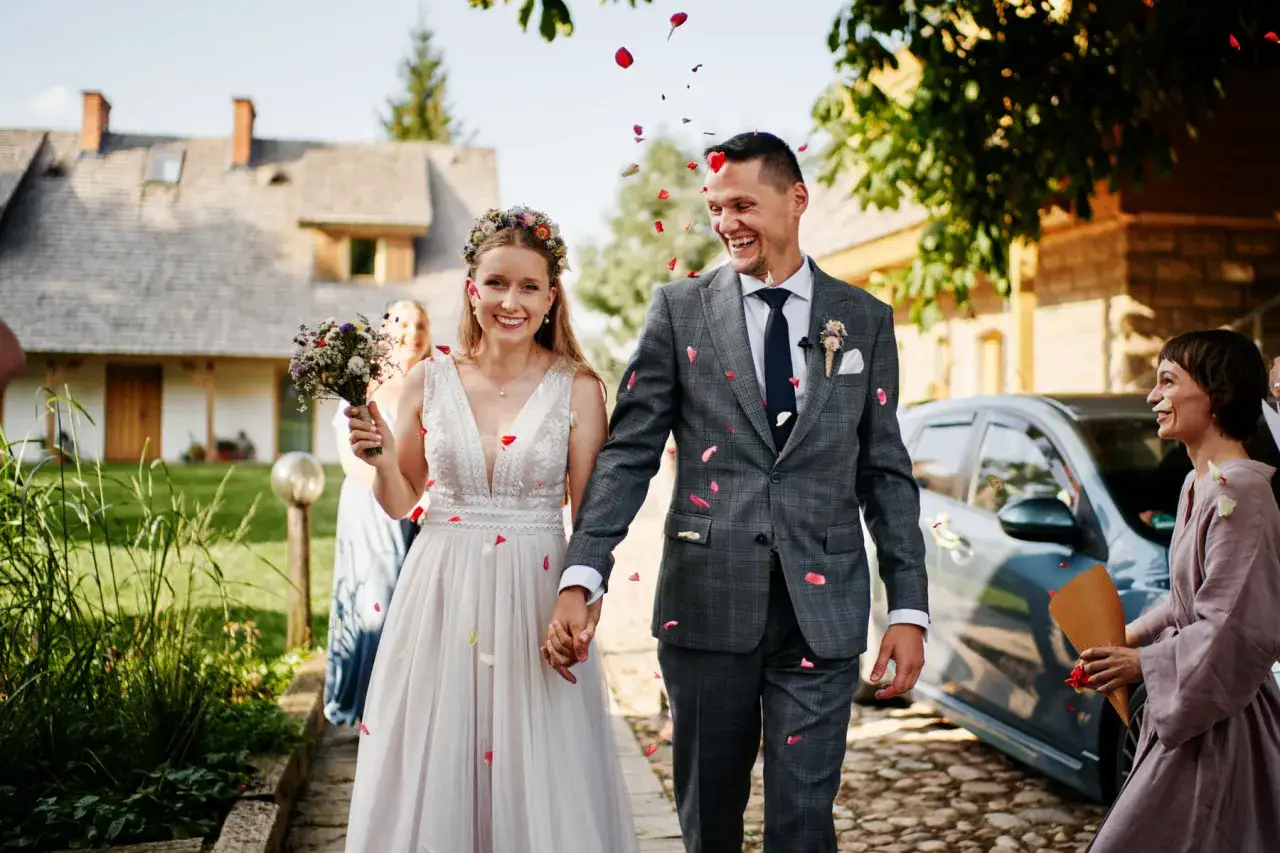Para młoda w luźnych, naturalnych strojach, z płatkami kwiatów w powietrzu, idzie ścieżką. Różnica między weselem w mieście a weselem 