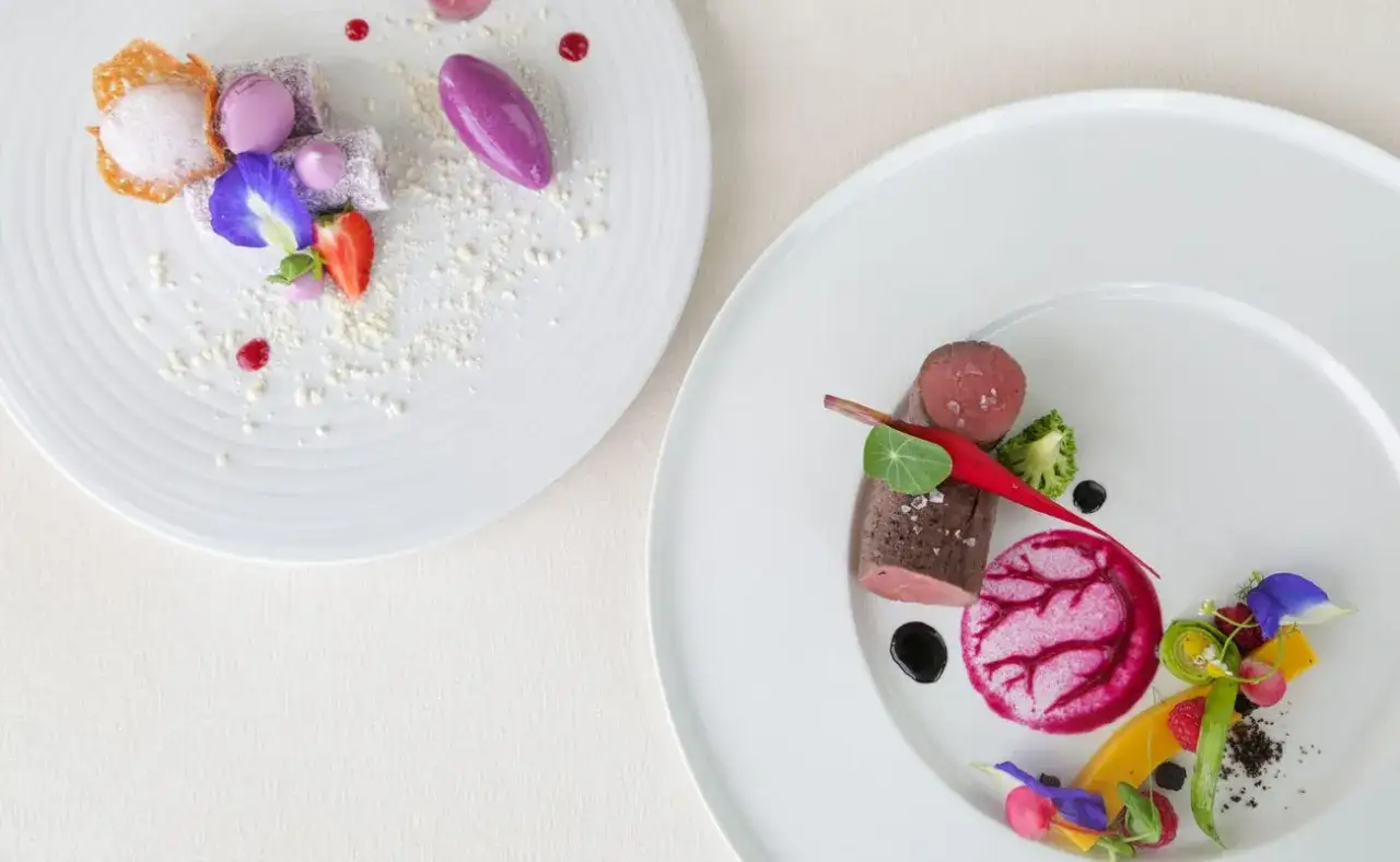 Eleganckie dania na dużych imprezach: fine dining wymaga precyzji. Na talerzach: mięso z warzywami i deser z owocami.
