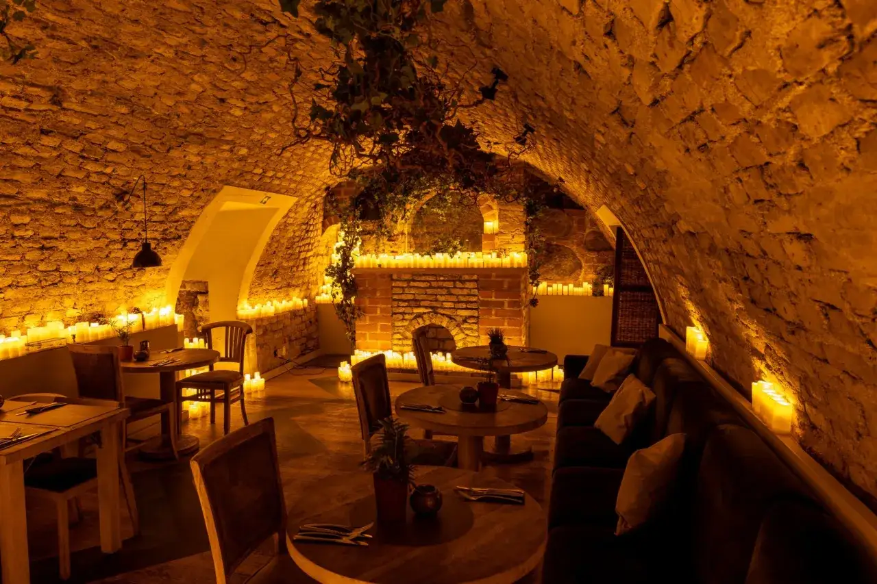 Kameralne wnętrze restauracji z kamiennymi ścianami, oświetlone licznymi świecami.