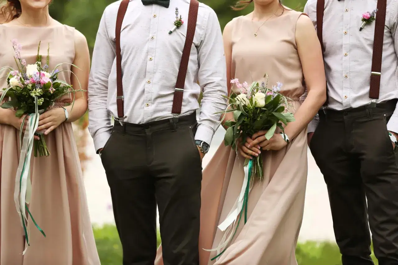 Eleganckie zaproszenie bez informacji o dress codzie. Panie w beżowych sukniach, panowie w koszulach, szelkach i brązowych spodniach.