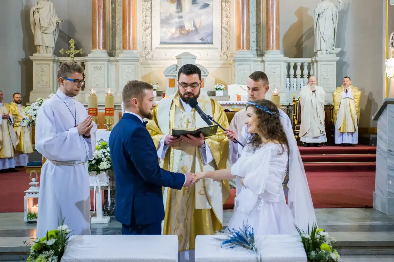 Para młoda trzyma się za ręce podczas ceremonii w kościele. Czy ślub cywilny to grzech? Pytanie to nurtuje wielu, ale tu widzimy sakrament małżeństwa.