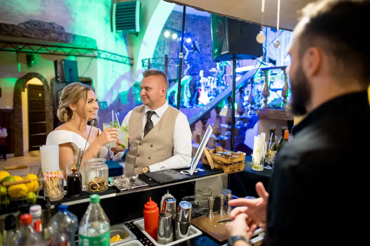 Para Młoda cieszy się drinkami przy barze. Czy warto inwestować w barmana i drink bar na weselu? Koszty a efekt - warto rozważyć!