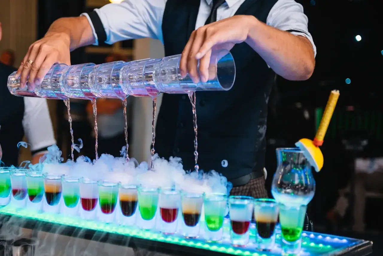 Barman nalewa kolorowe shoty, tworząc efektowny pokaz. Czy warto inwestować w barmana i drink bar na weselu? Koszty a efekt - warto rozważyć!