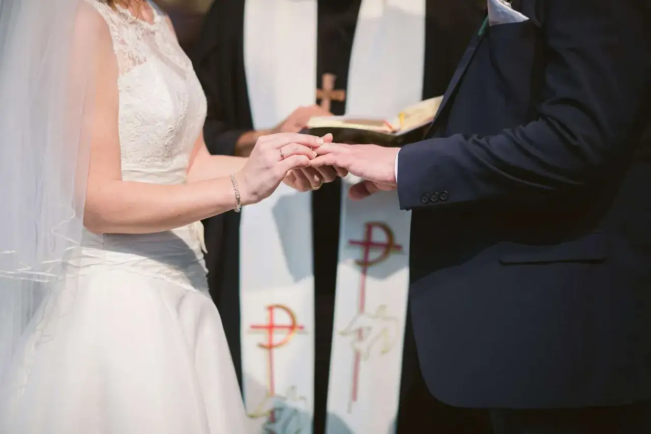Para ślubna wymienia obrączki podczas ceremonii. Czy do ślubu potrzebne jest świadectwo religii? Duchowny błogosławi parę.