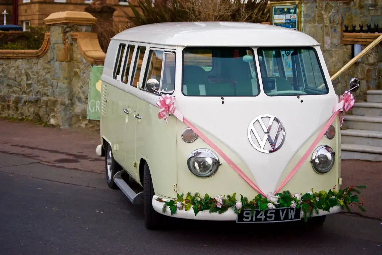Stylowy VW Transporter, ozdobiony różową wstążką i kwiatami, idealny do zaplanowania logistyki transportu i noclegu dla gości przyjezdnych.